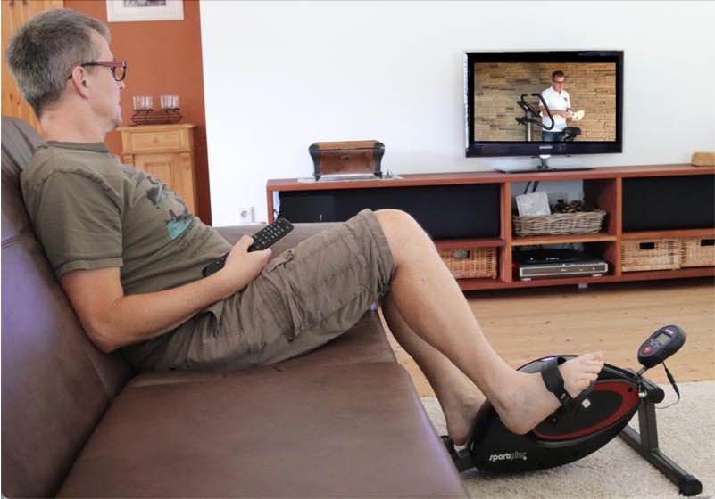 Das Bild zeigt das Training mit einem Mini-Heimtrainer vor dem Fernseher.